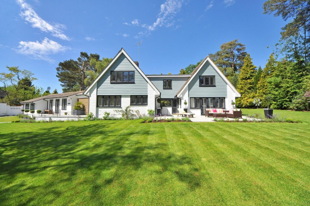 A white and gray wooden house near grass field and trees.